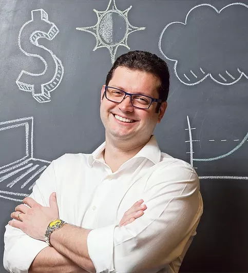 Rodolfo Simões de braços cruzados diante de um quadro com desenhos de cifrão, nuvem e gráfico